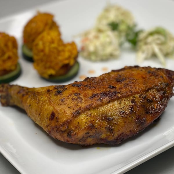A Posi's Kitchen African dish with a large roasted chicken leg, fried fritters, and coleslaw.