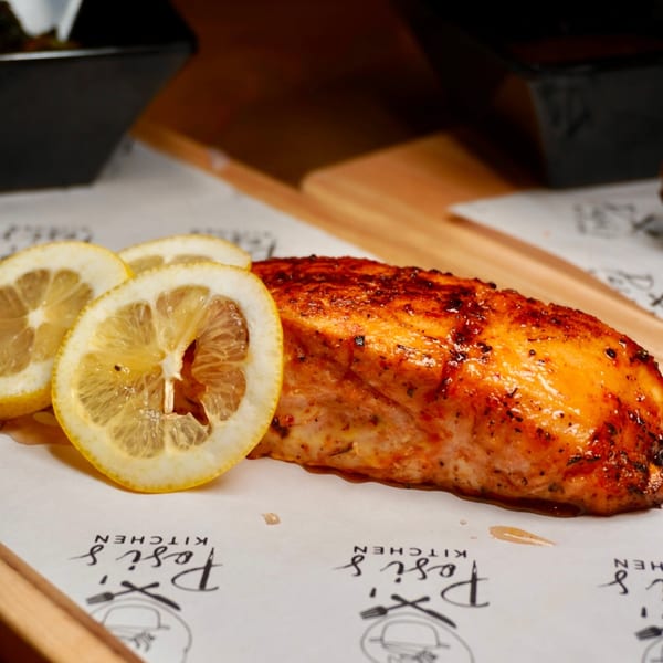 A perfectly cooked salmon fillet with a crispy skin, garnished with fresh lemon slices on Posi's Kitchen branded paper.