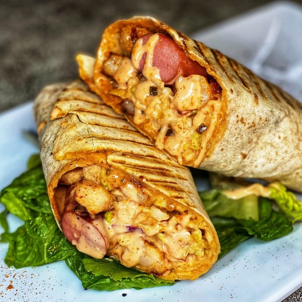 Two grilled African wraps, filled with chicken, sausage, and creamy sauce, on a bed of lettuce.